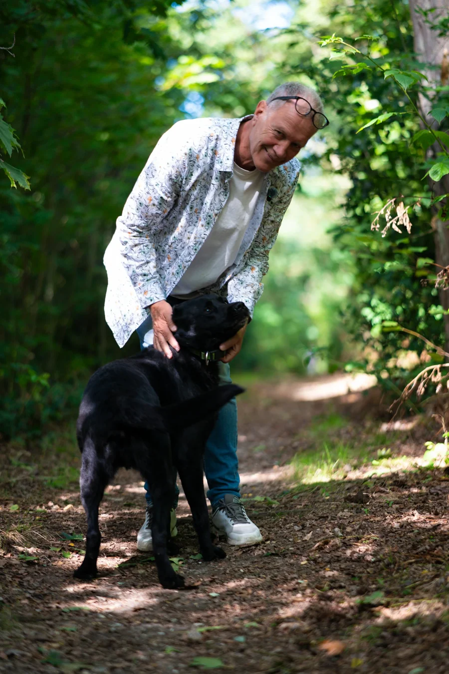 Thomas Schimmeck auf einem Waldweg, gebückt, mit seinem schwarzen Hund